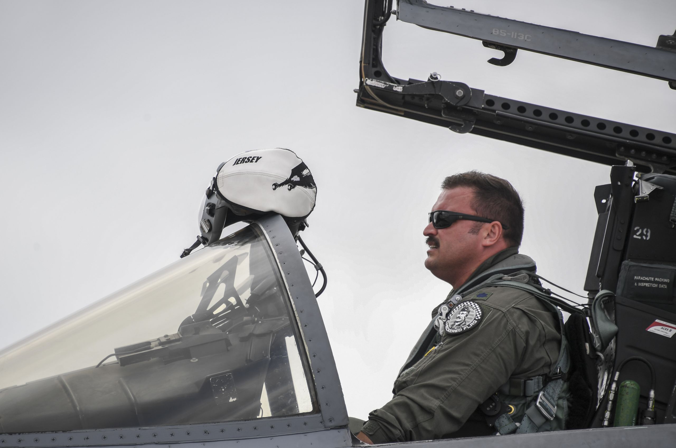 A pilot sits in the cockpit of a jet with the hatch open