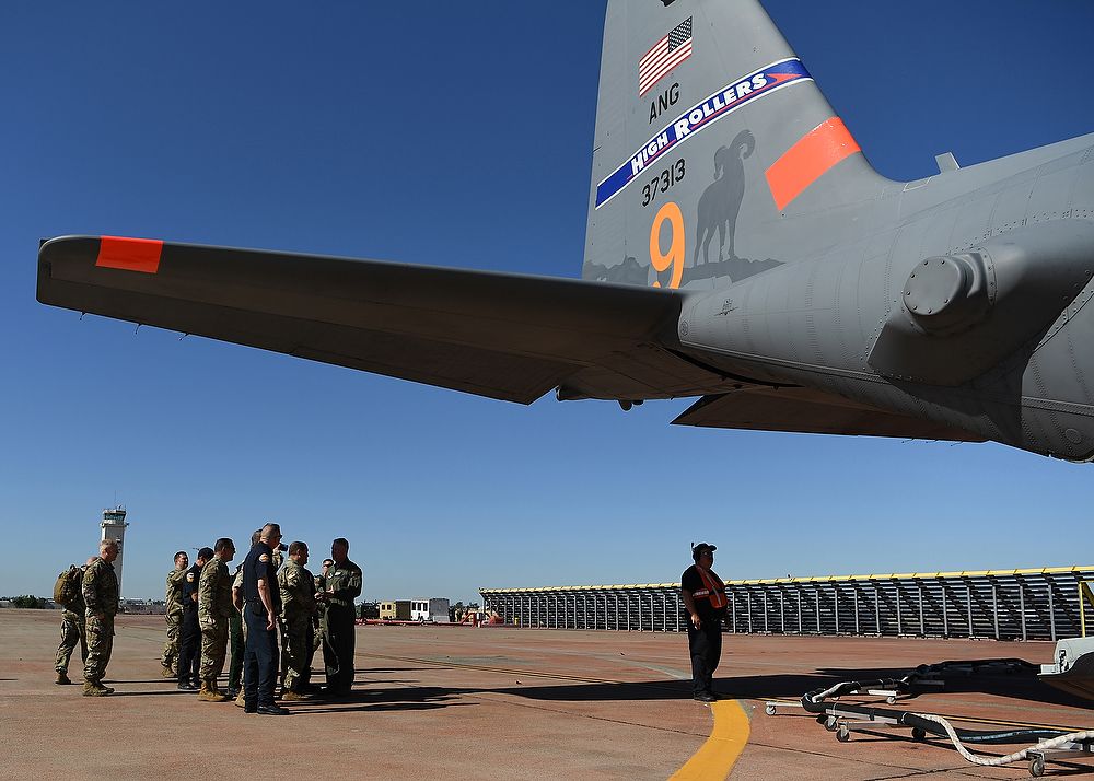 Group of people stand under tail of airplane.