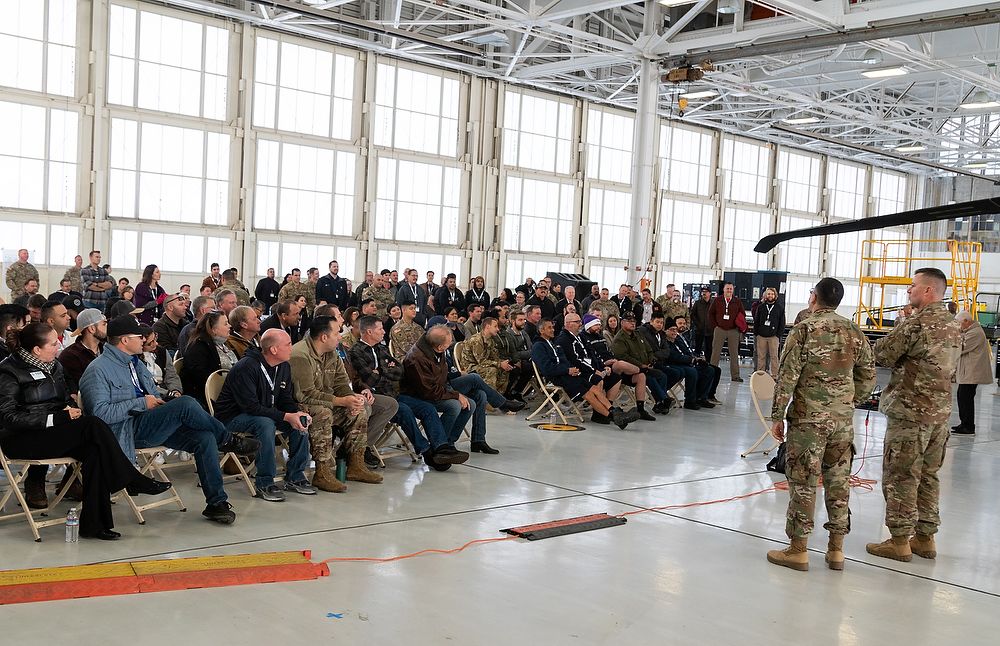 Crowd of civilians sit in hangar.