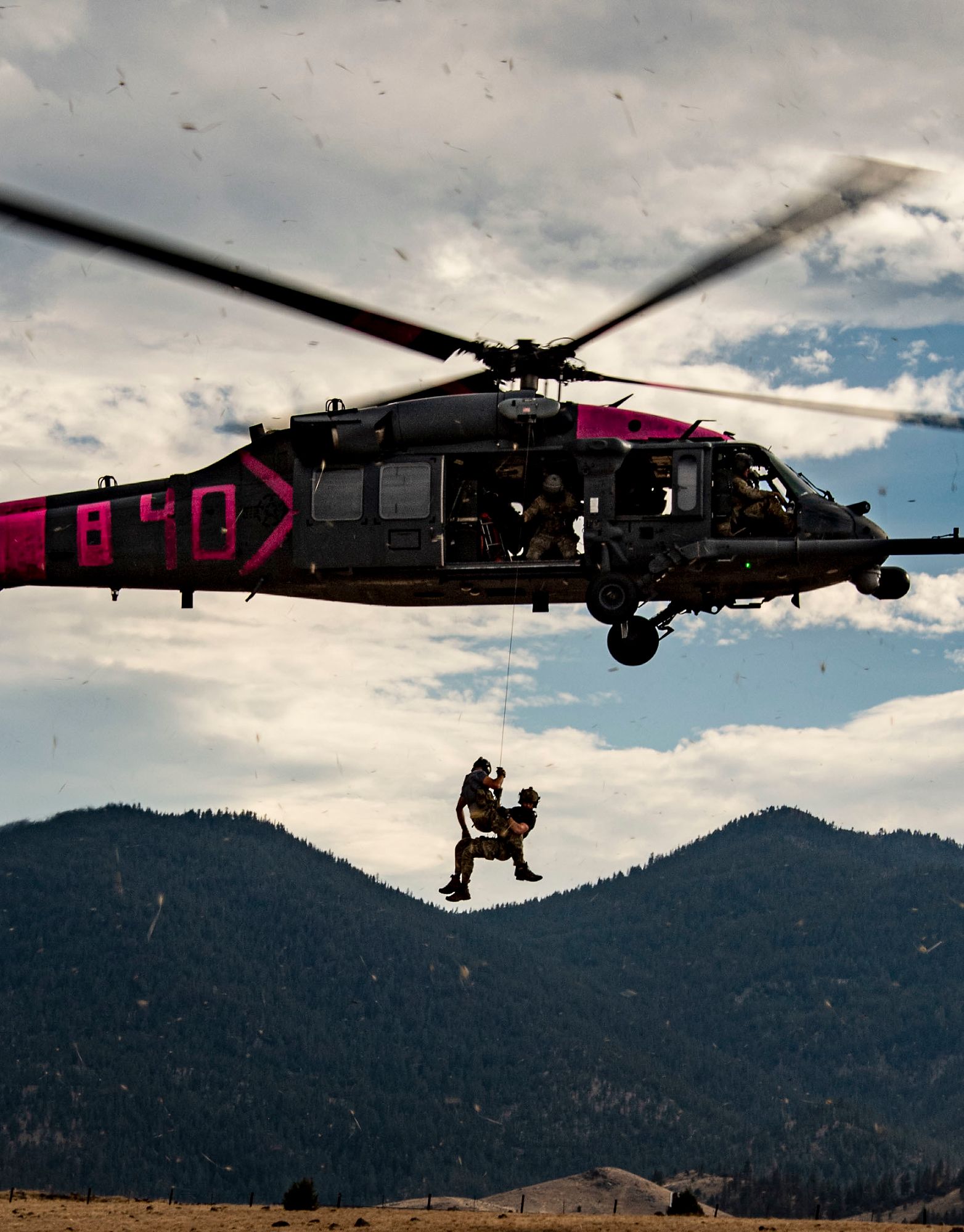 Men hang from rope out of helicopter.