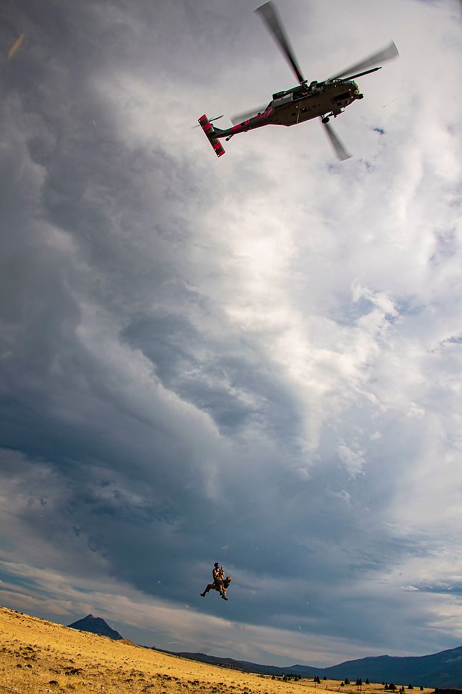 Men hang from rope out of helicopter.