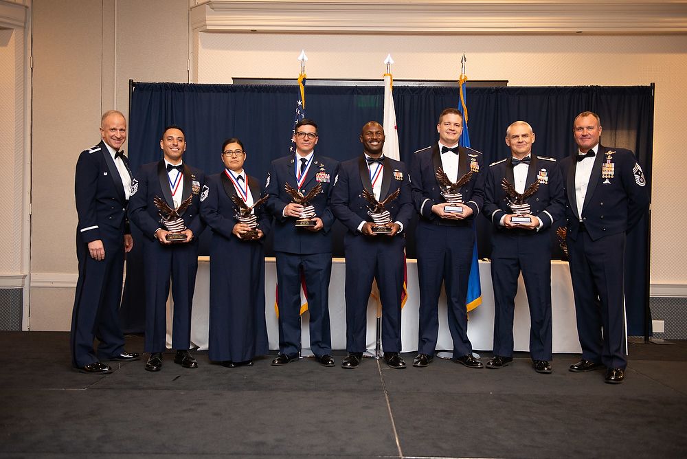 Airmen in dress uniforms hold trophies.