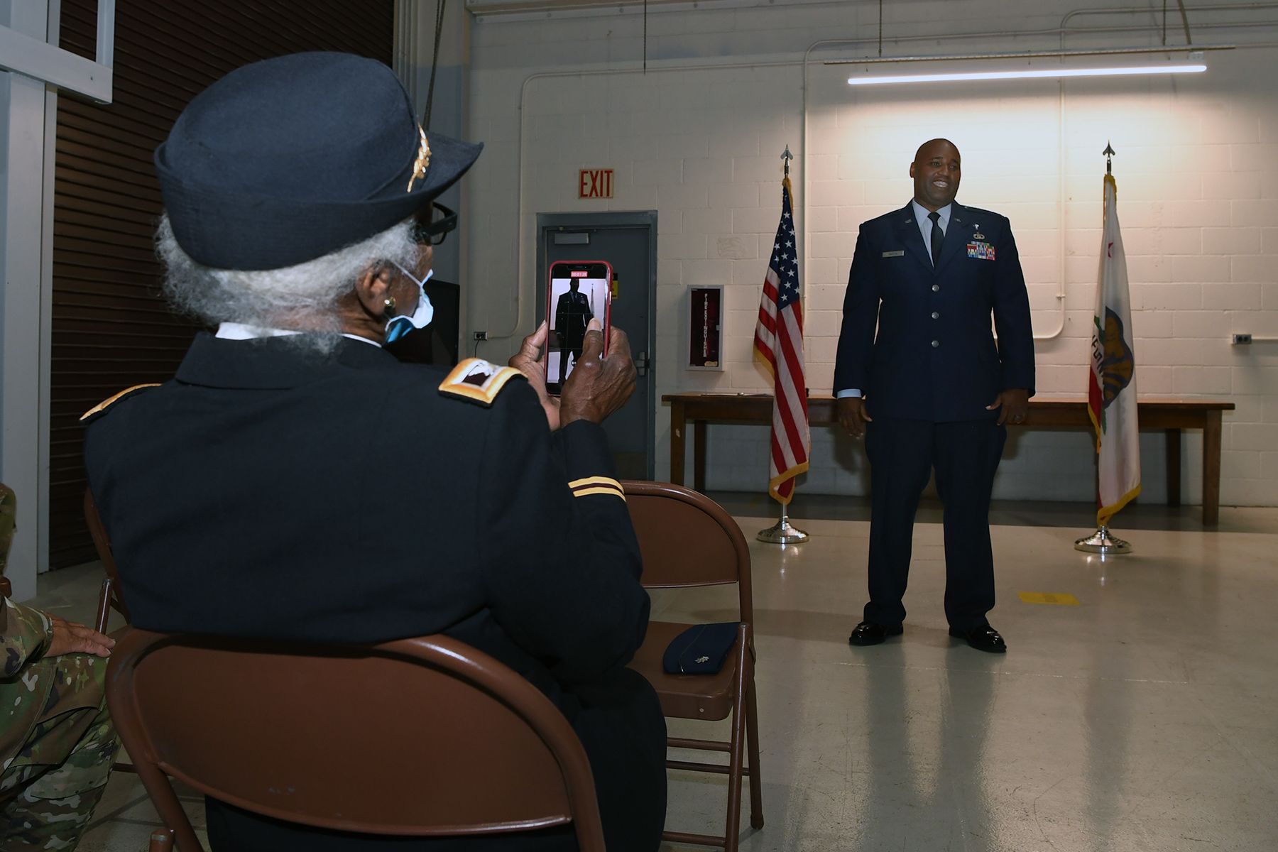Woman in Army uniform takes photo on cell phone.
