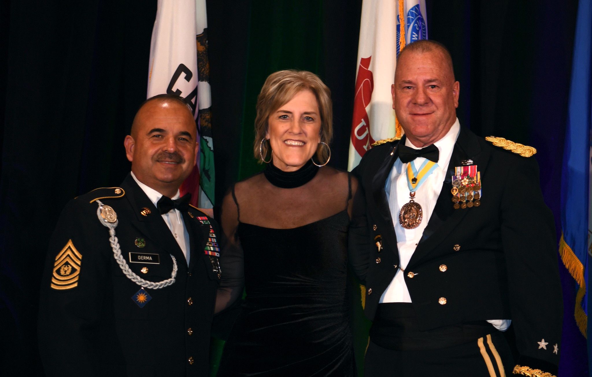 A woman in formal dress poses for a photo with two Soldiers in Army dress uniform.