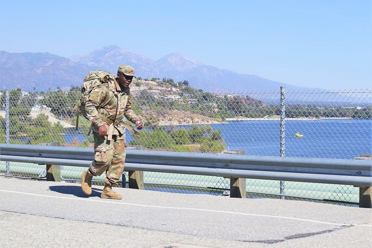Soldier walks on shoulder of a road with weighted backpack.