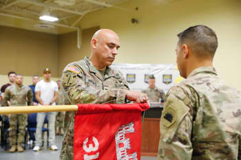 A Soldier attaches a ribbon to a unit flag