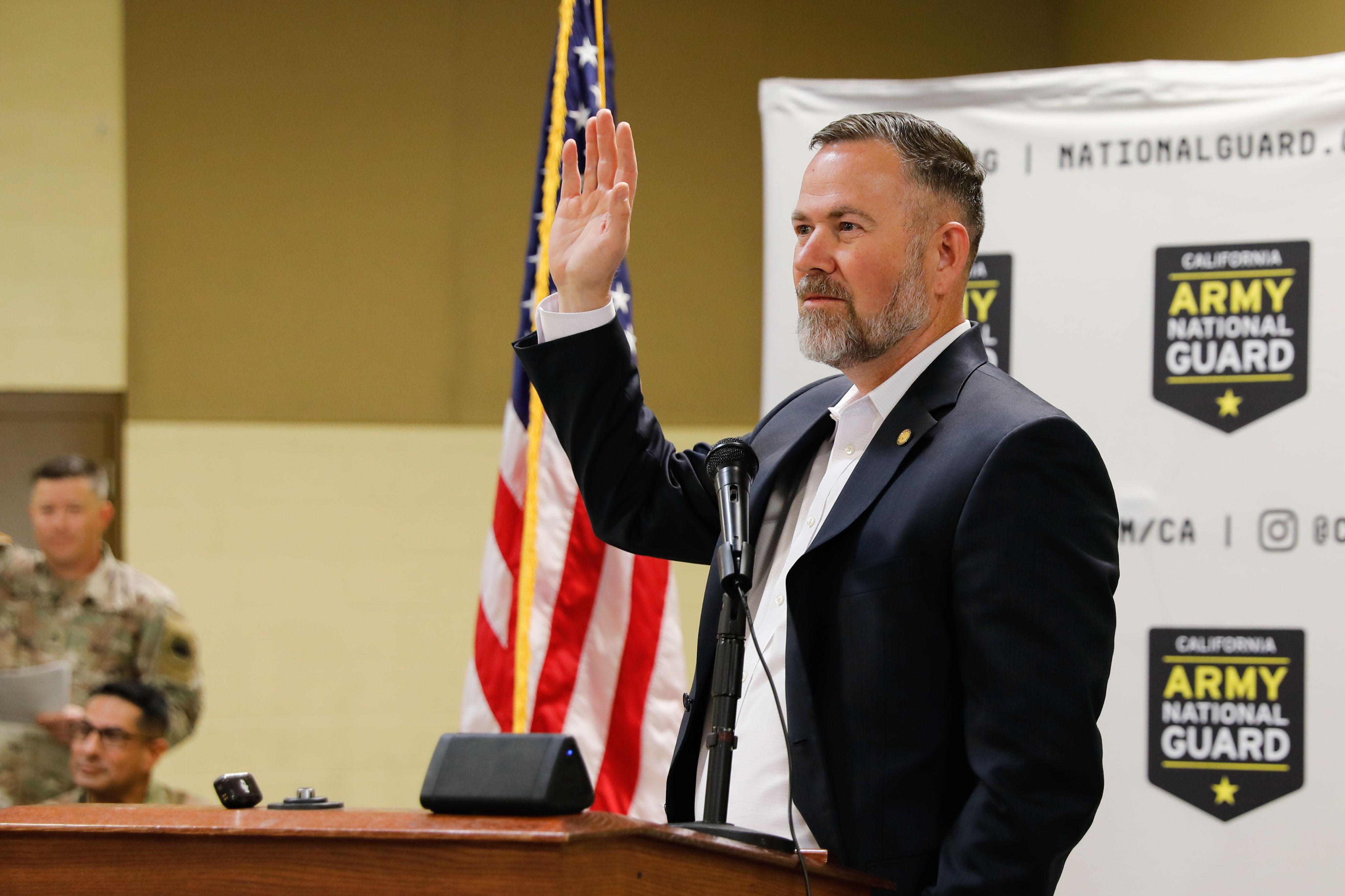 A man in a suit raises his hand while speaking to Soldeirs