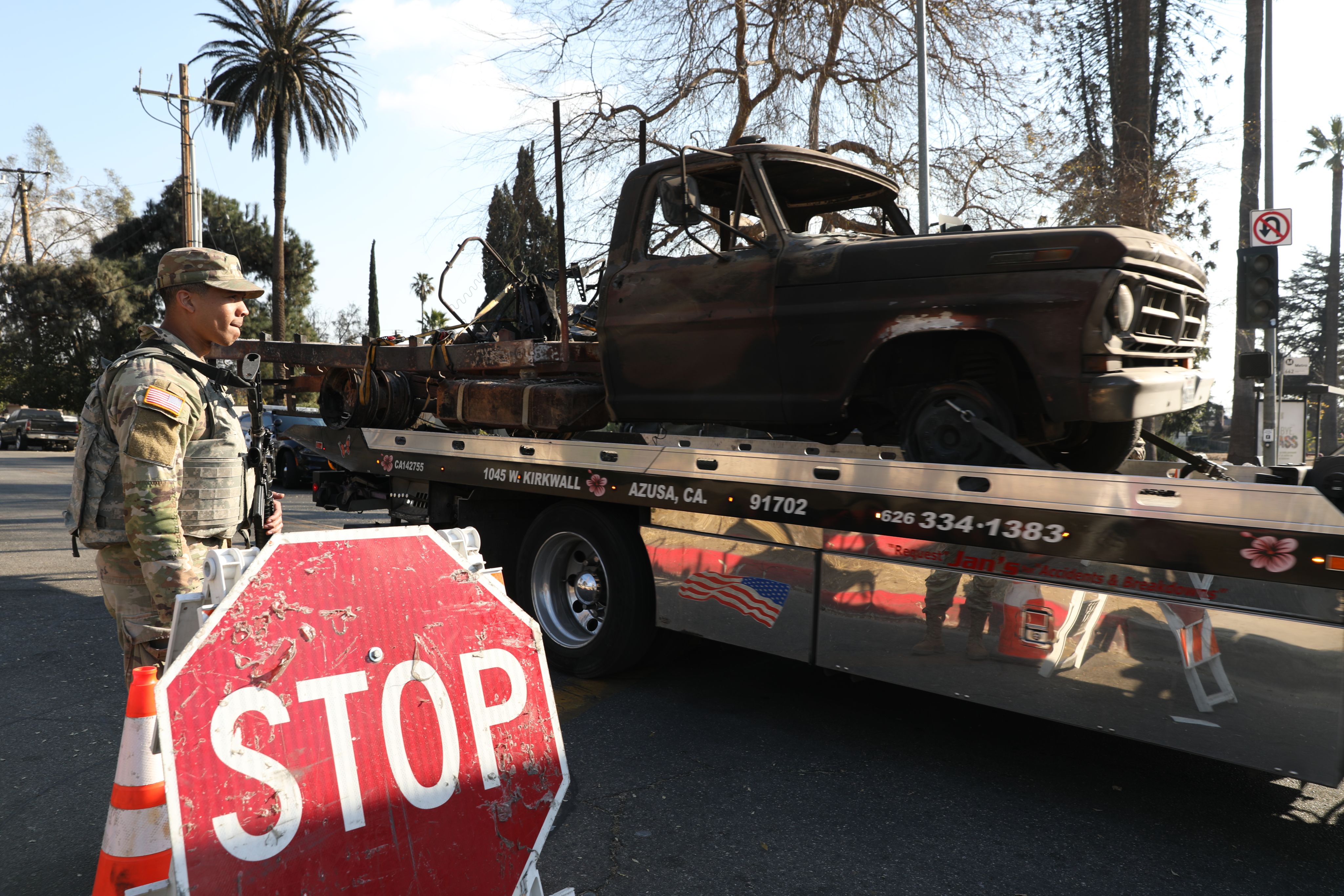 A Soldier stands aside as a trailer carrying a burnt truck passes.