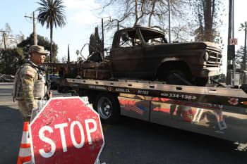 A Soldier stands aside as a trailer carrying a burnt truck passes.