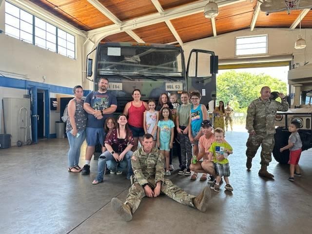 Adults and children gather around military truck