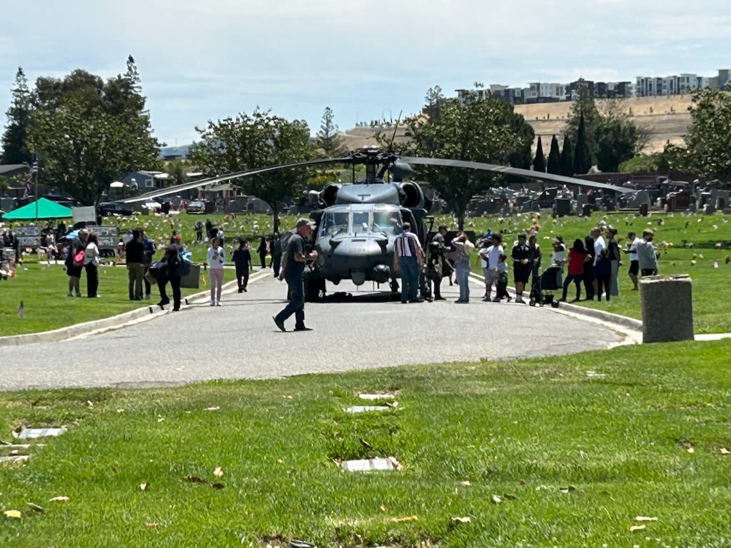 A helicopter sits in the road at the ceremony, surrounded by dozens of people observing the inside and outside of the craft.