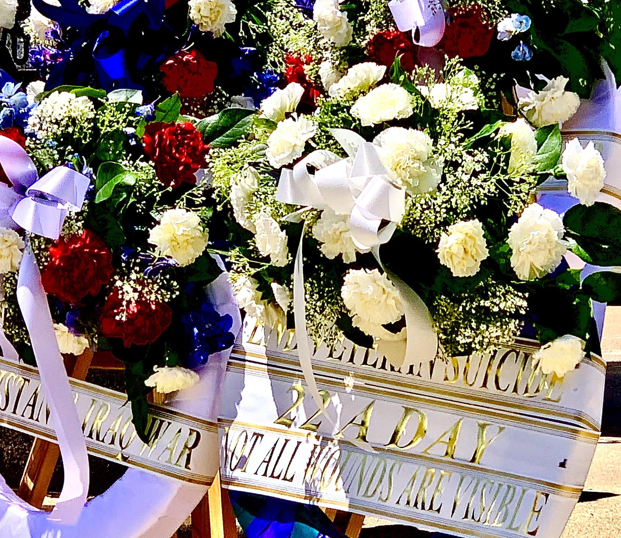 A colorful wreath with flowers and white ribbon is displayed, showing the title: "22 a Day. Not all wounds are visible."