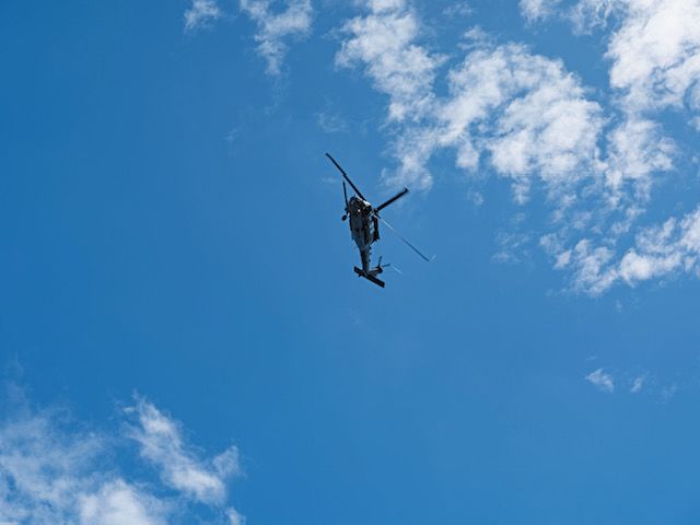 A grey helicopter is pictured from below and is shown flying in the blue sky.