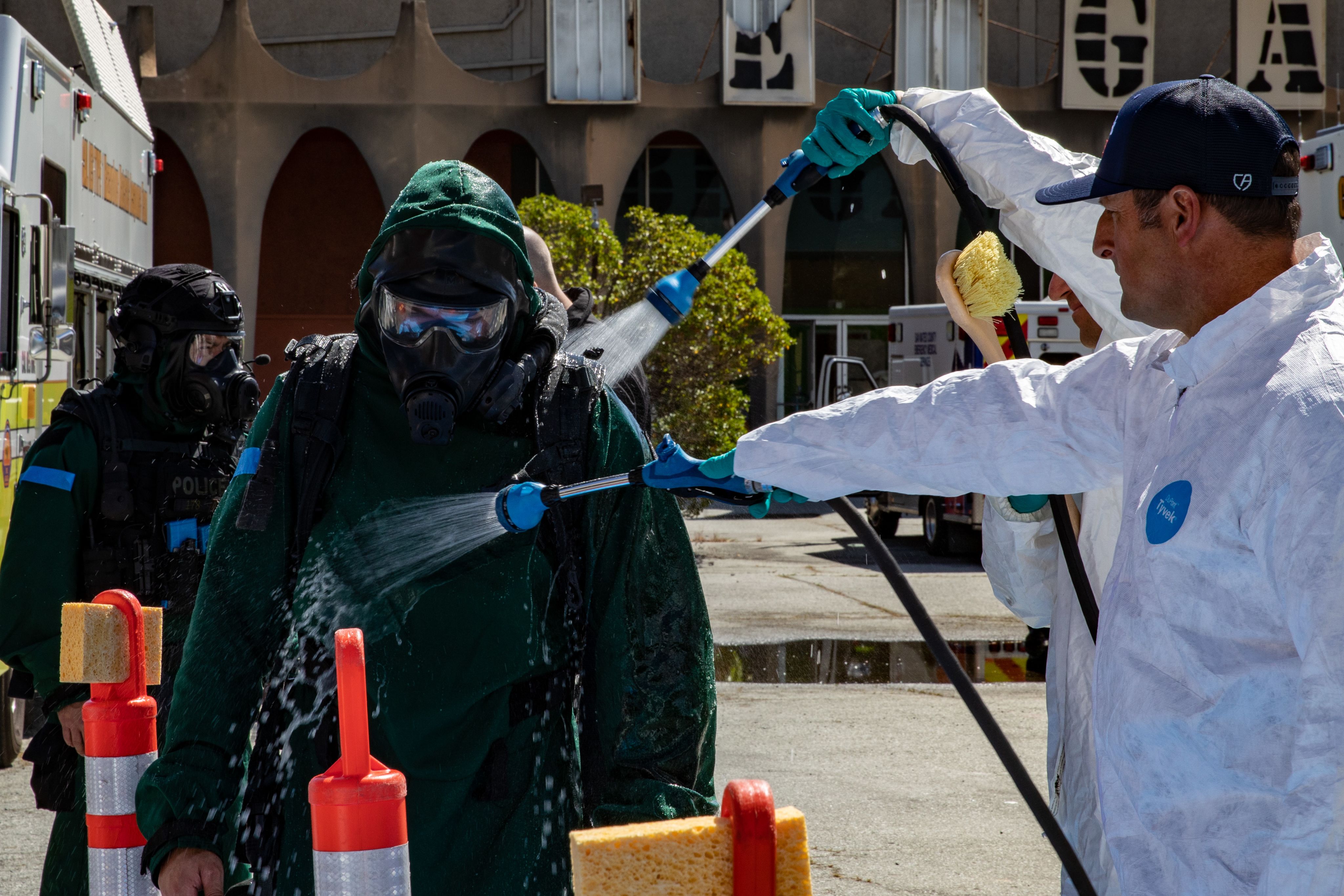 A service member in a green HAZMAT suit gets hosed down