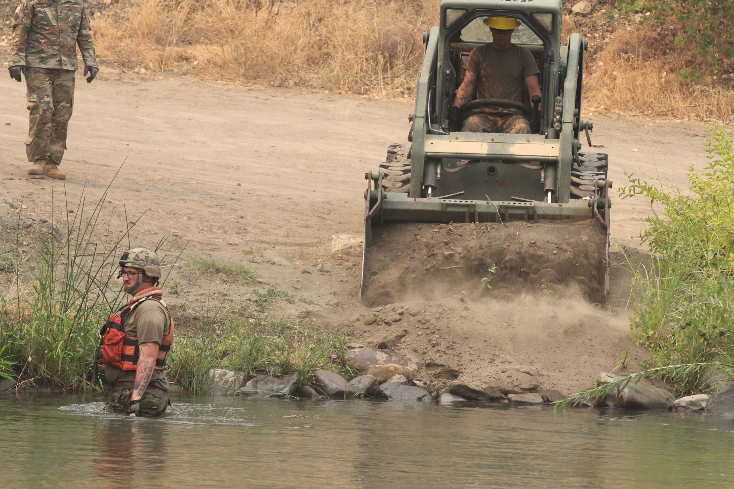 Soldier drives a Bobcat tractor with dirt to smooth out area bridge ramp will be built on.