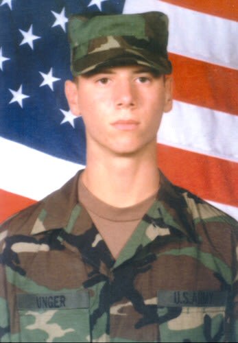 Soldier poses in front of American flag.
