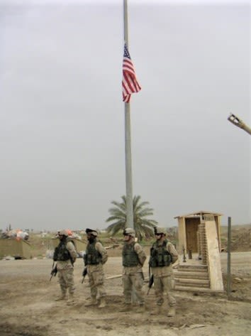 Four soldiers stand in front of an American flag flown at half-mast in Iraq.