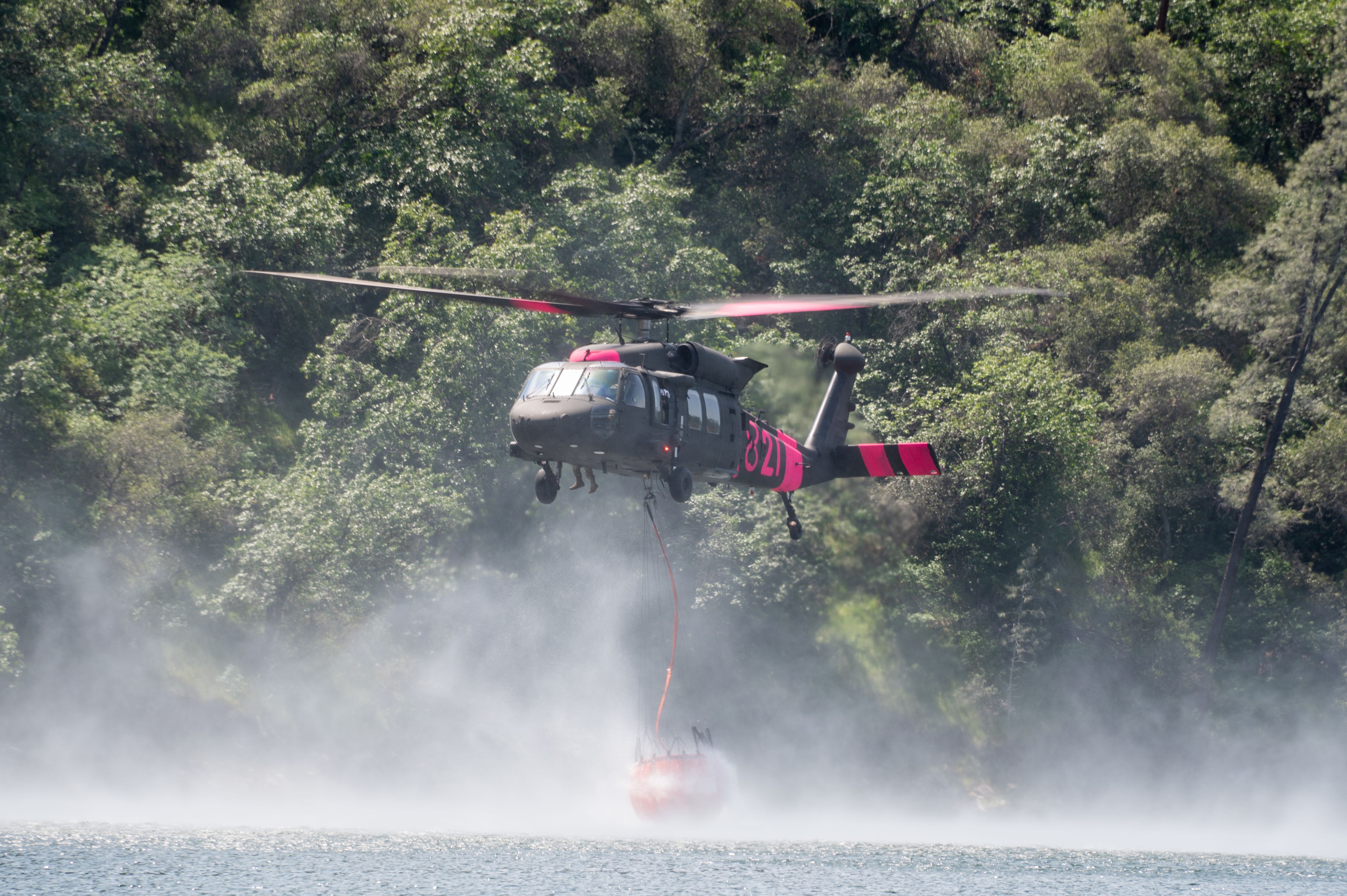 UH-60 Blackhawk helicopter lowering orange water bucket in lake
