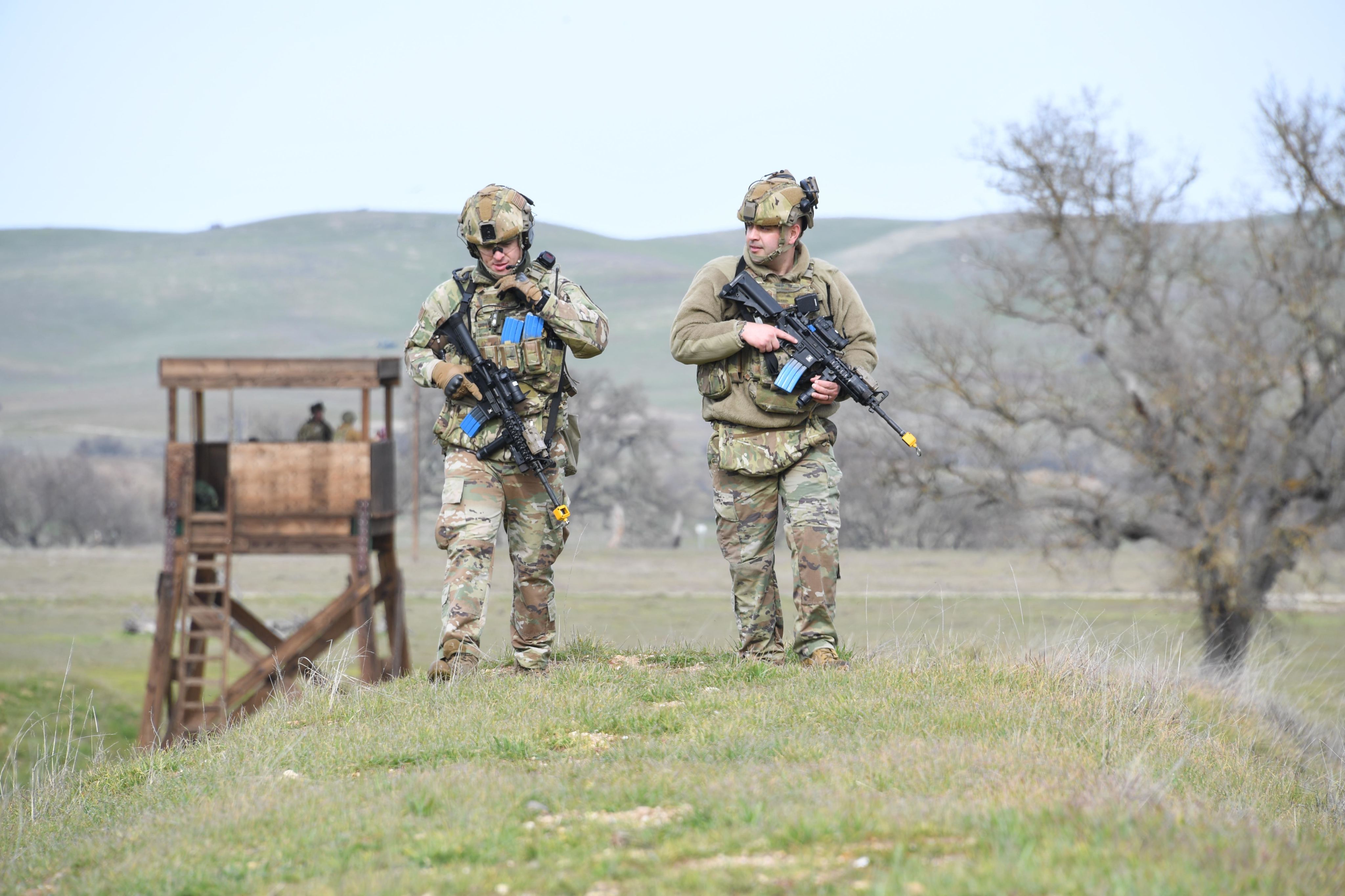 Airmen carry training weapons while walking in field.
