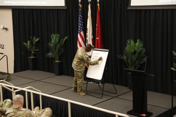 a man in uniform writes on a white board on a stage