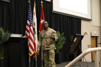a man in uniform speaks from a stage to the crowd