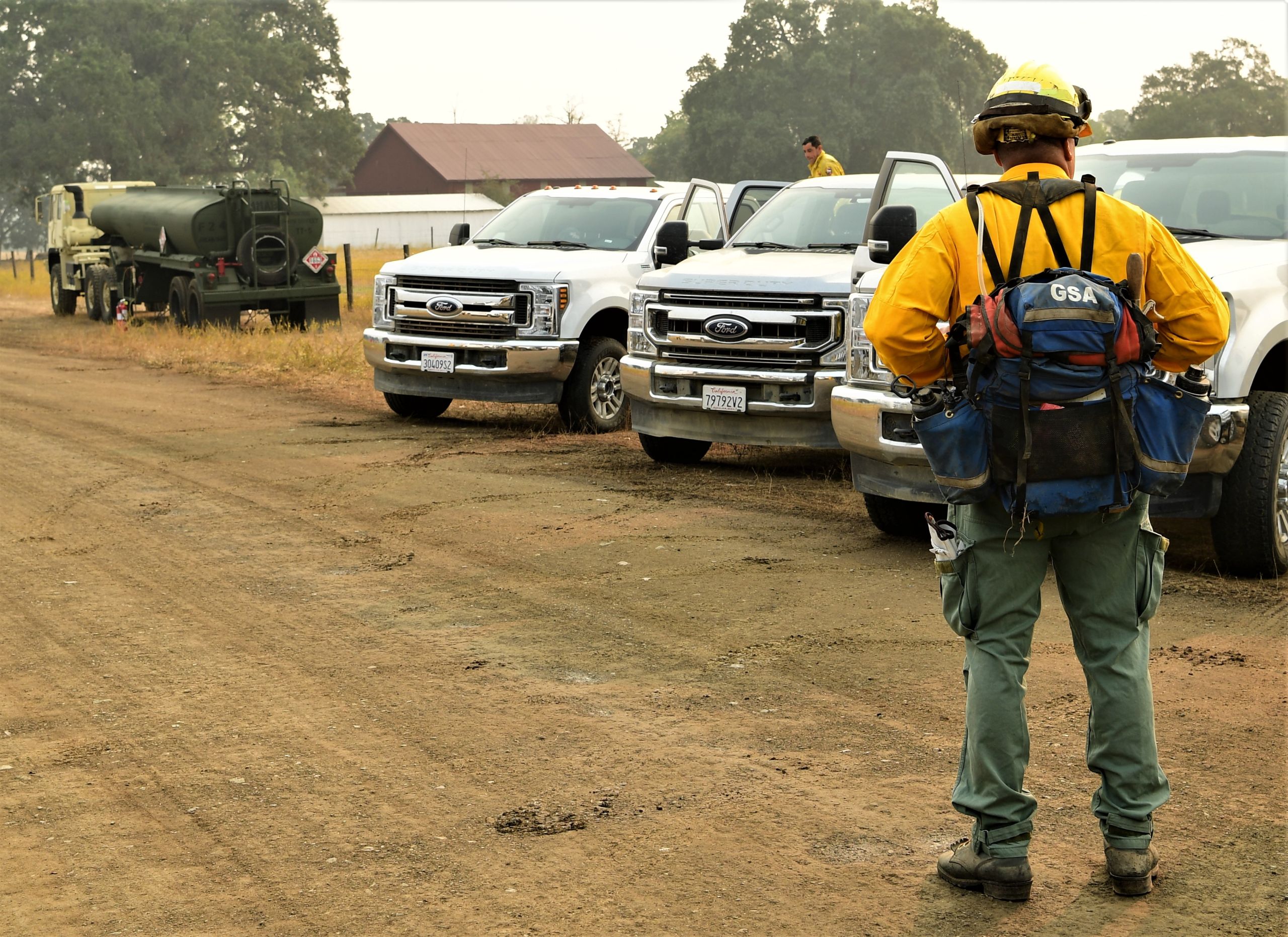 Service member in CAL FIRE wildland firefighting gear stand near work trucks.