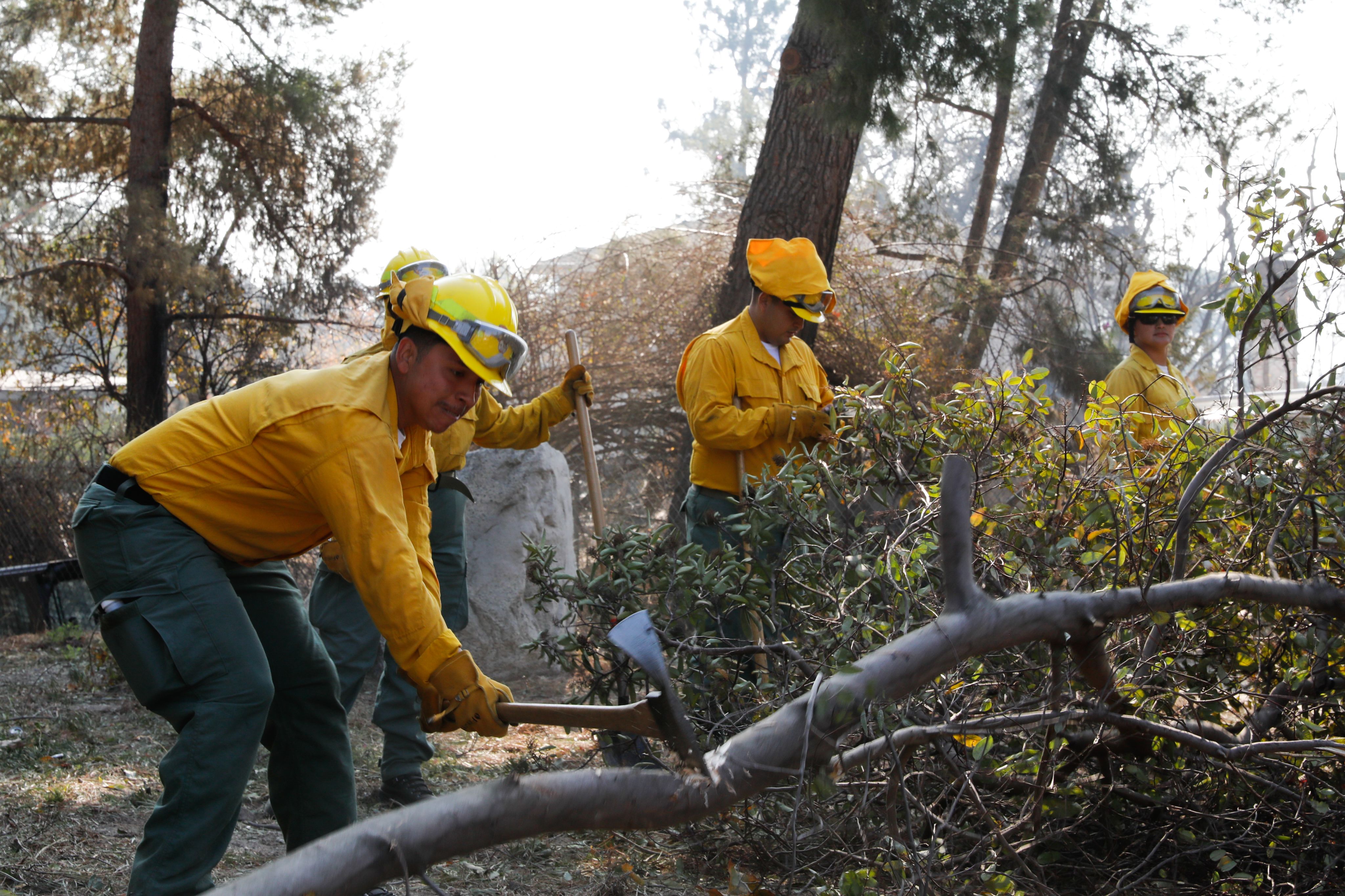 Soldiers wearing Nomex clean up debris from a wildfire with shovels in a neighborhood.