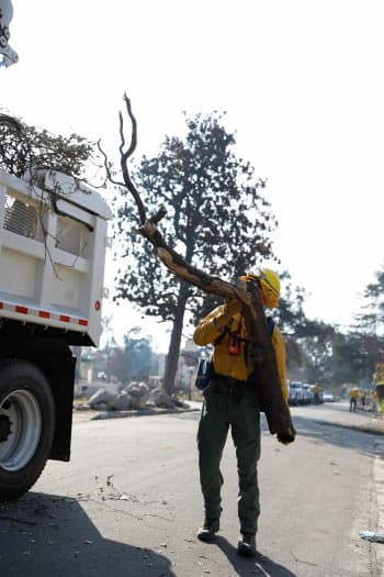 A Soldier wearing Nomex loads a log into a truck,