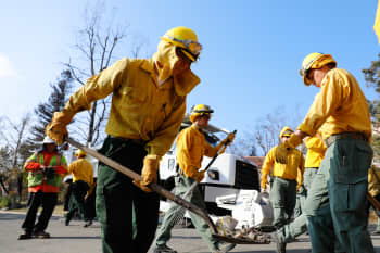 Soldiers wearing Nomex clean up debris from a wildfire with shovels in a neighborhood.