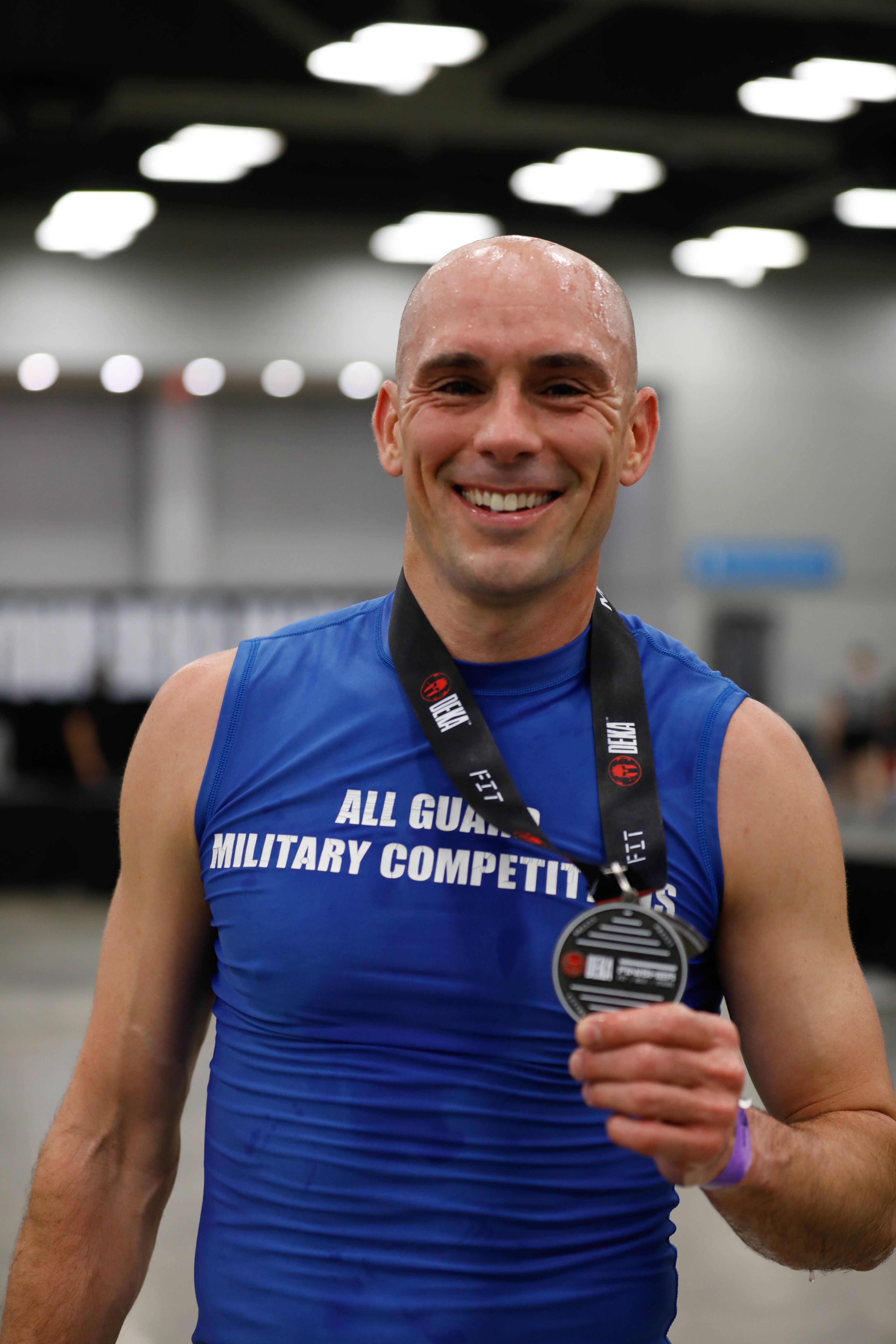 Man in blue tank top shows medal.