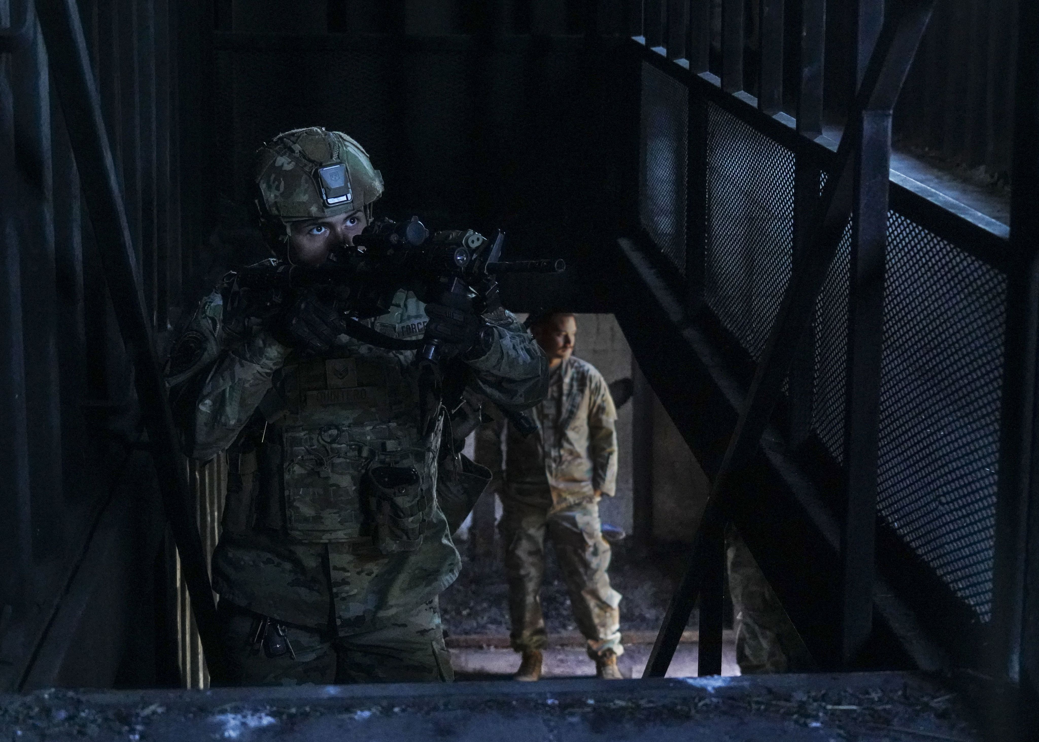 Airman with weapon climbs stairs.