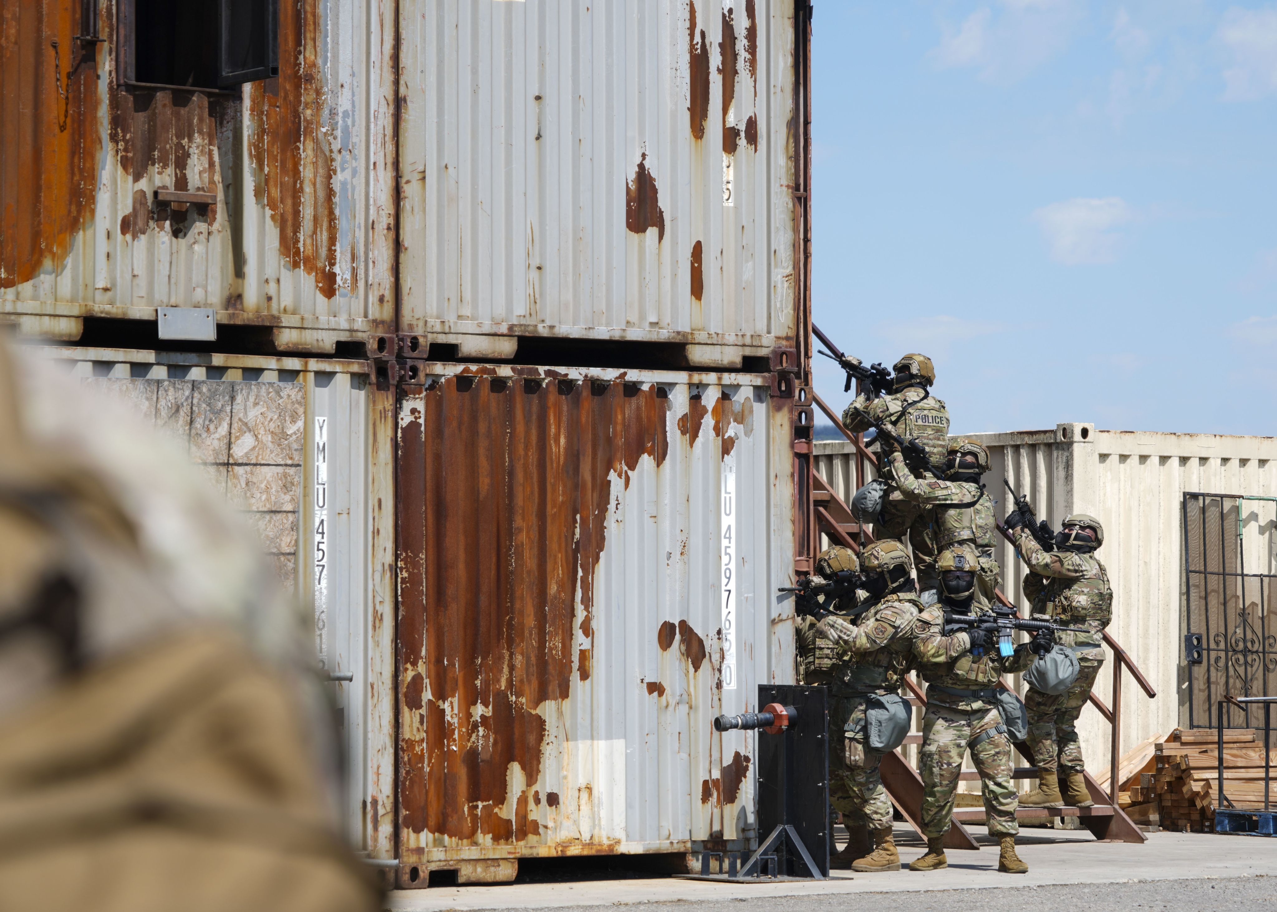 Airmen with weapons peek around shipping container.
