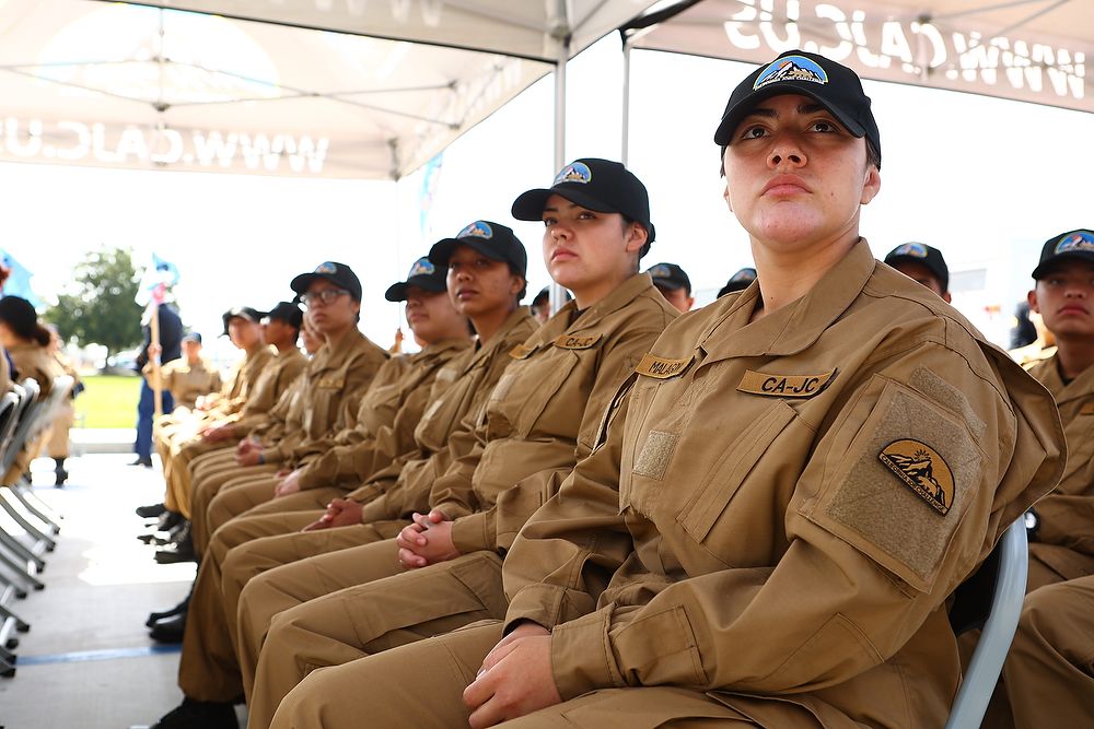 Teen girls in uniform sit in chairs.
