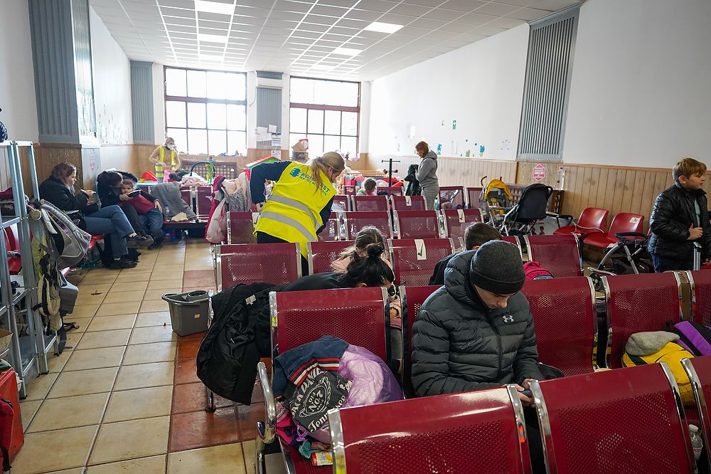 People sit in a train station with red seats.