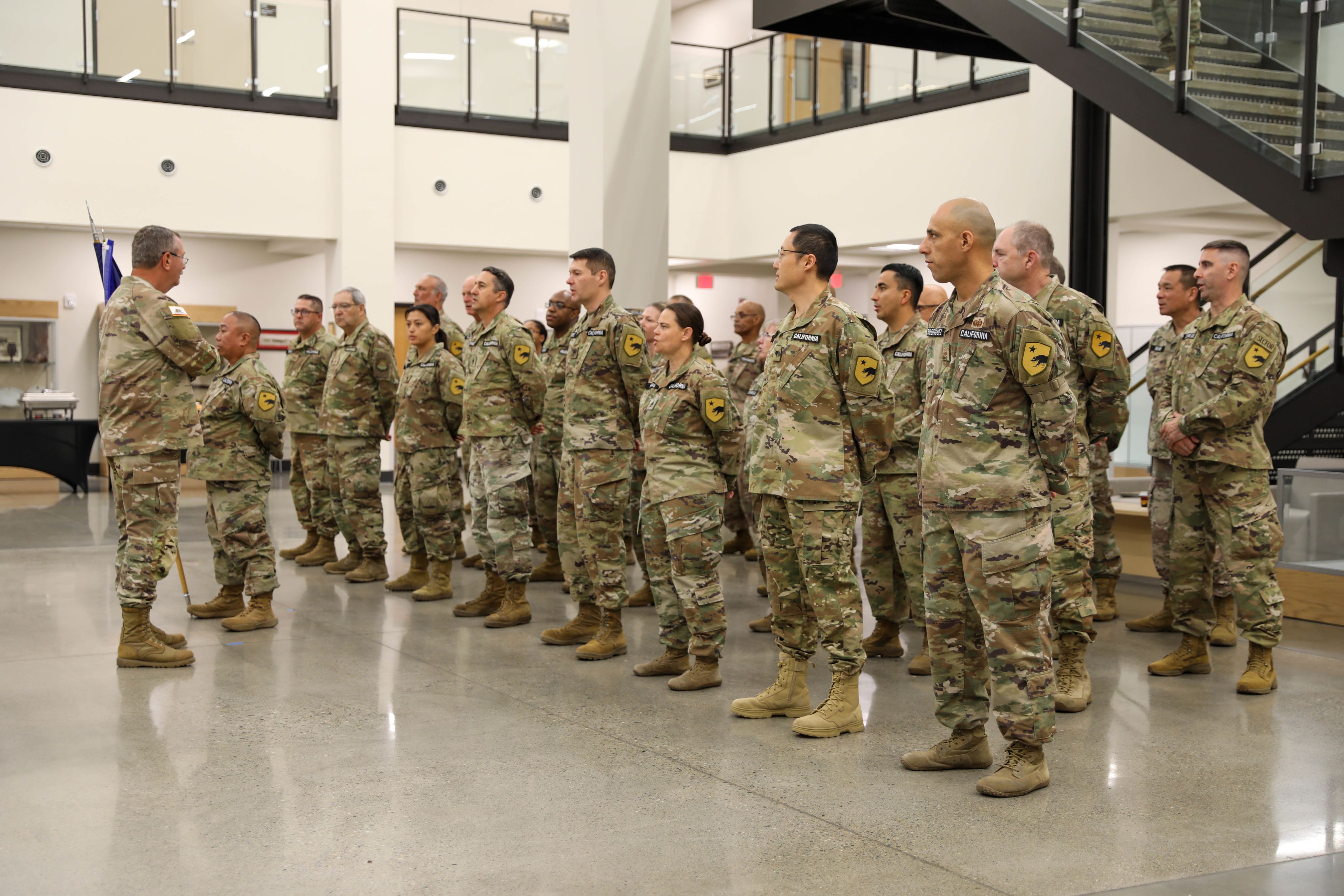 A man in uniform speaks to a group of uniformed Soldiers in formation