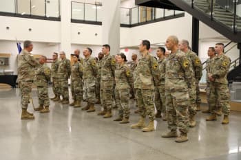 A man in uniform speaks to a group of uniformed Soldiers in formation