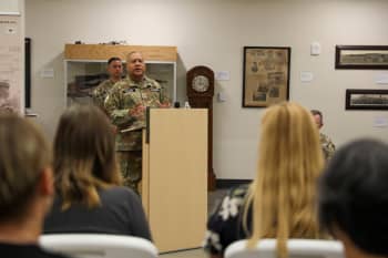 A man in uniform speaks from behind a podium to an audience