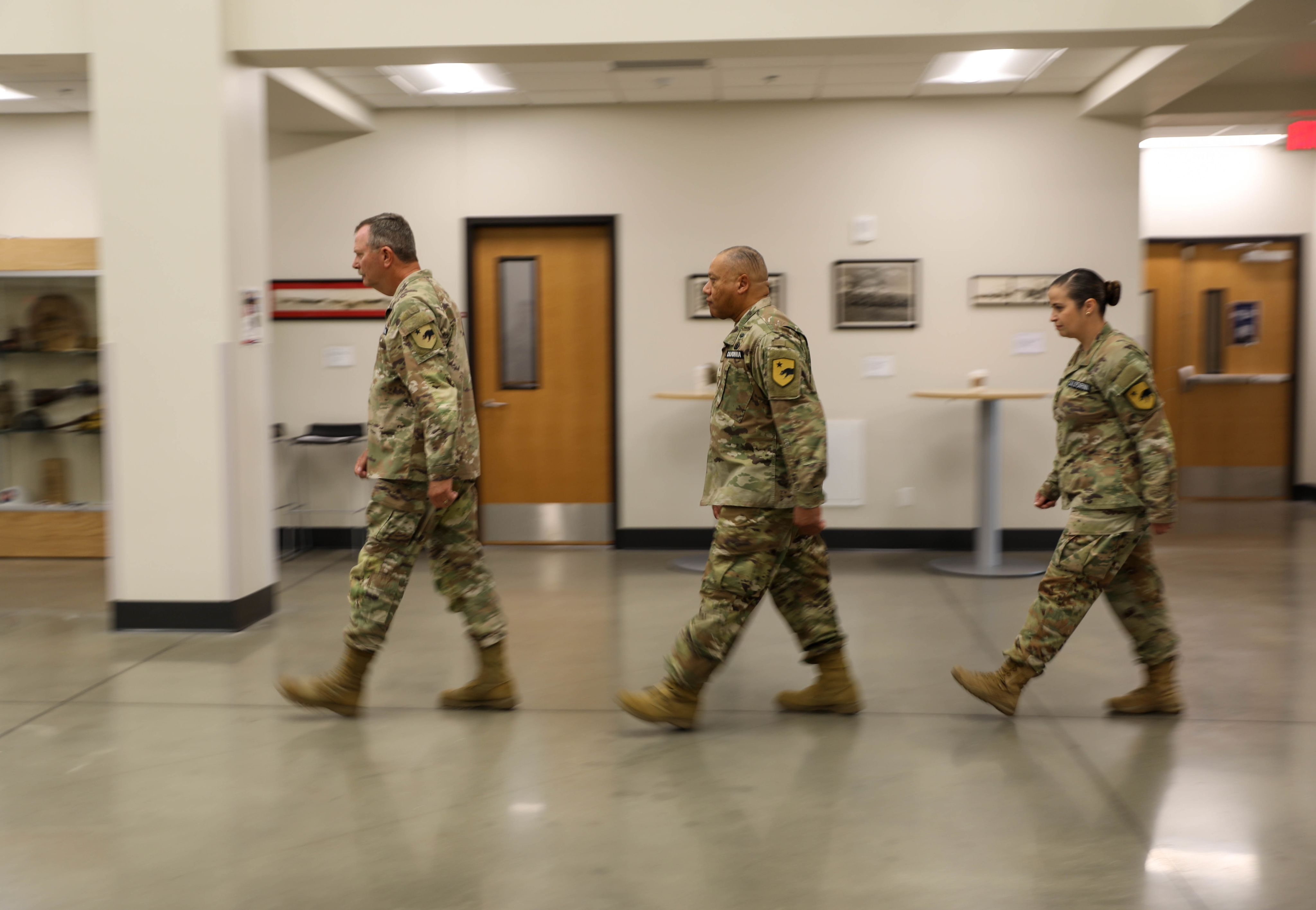 Three people in uniform march in a file across an atrium