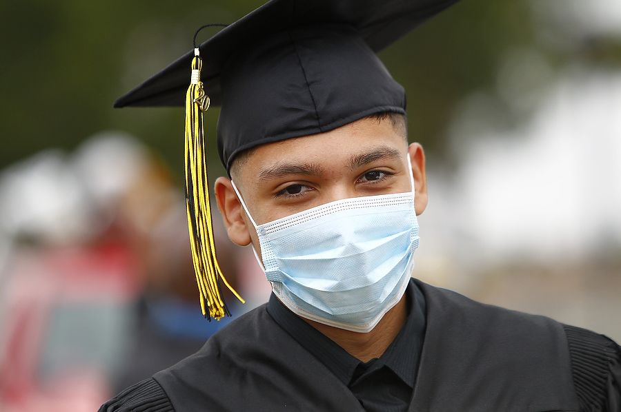 A student in black graduation cap and gown with blue face mask on.