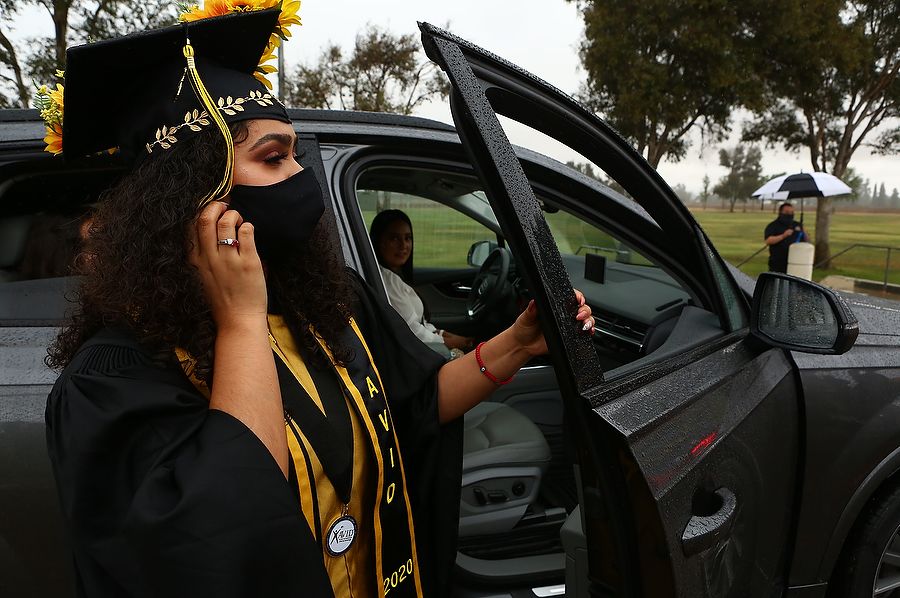 Student in graduation cap and gown secures her face mask