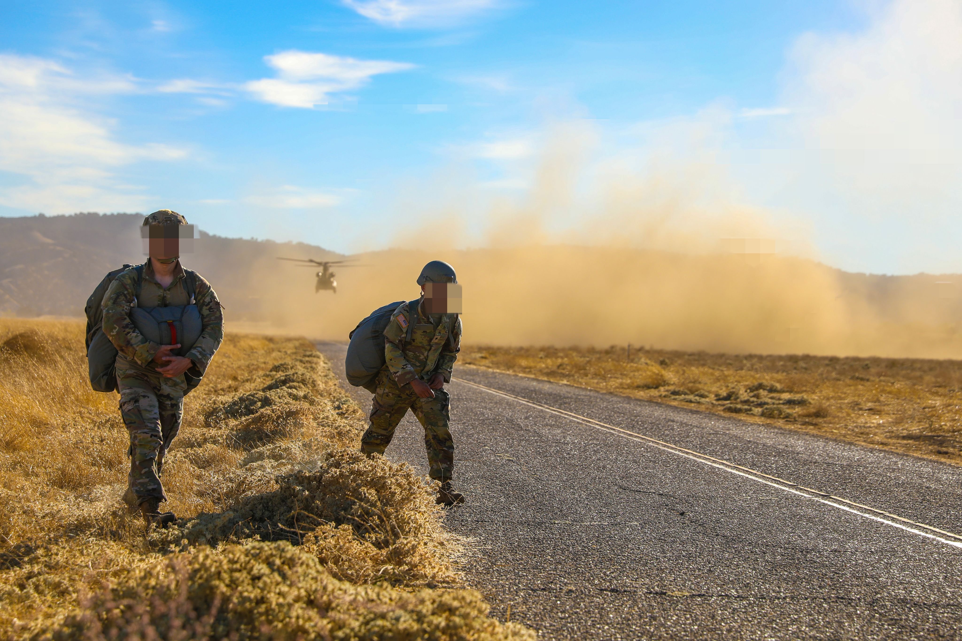 Two Special Forces Soldiers walk through dust, away from helicopter taking off
