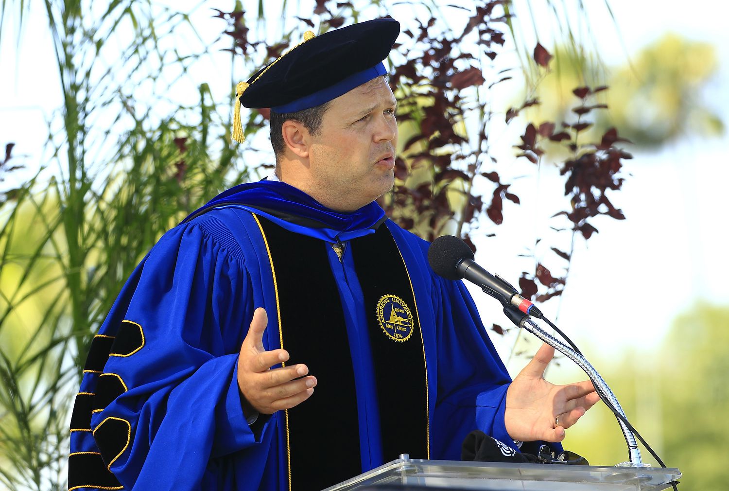 Man in doctoral regalia speaks.
