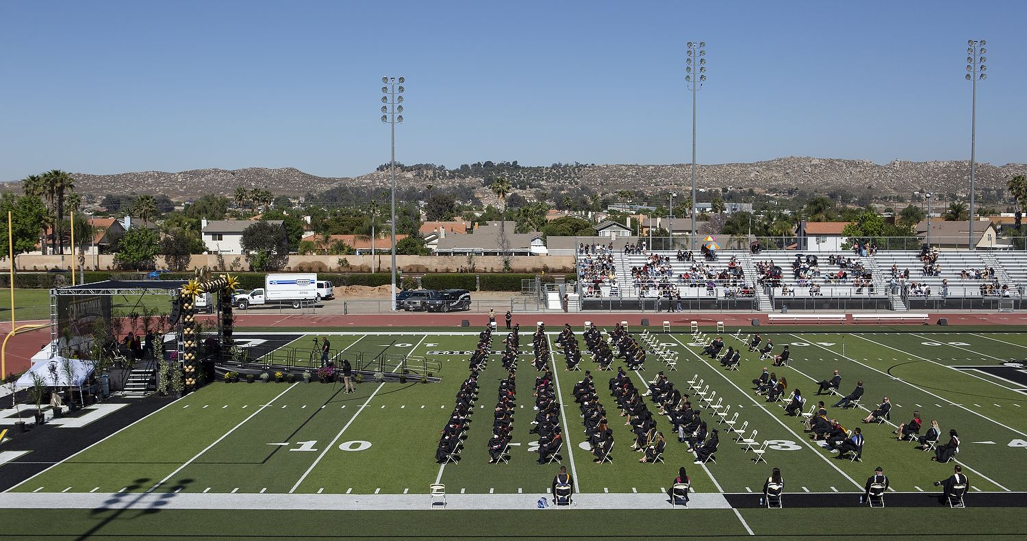 Graduates in chairs on football field.