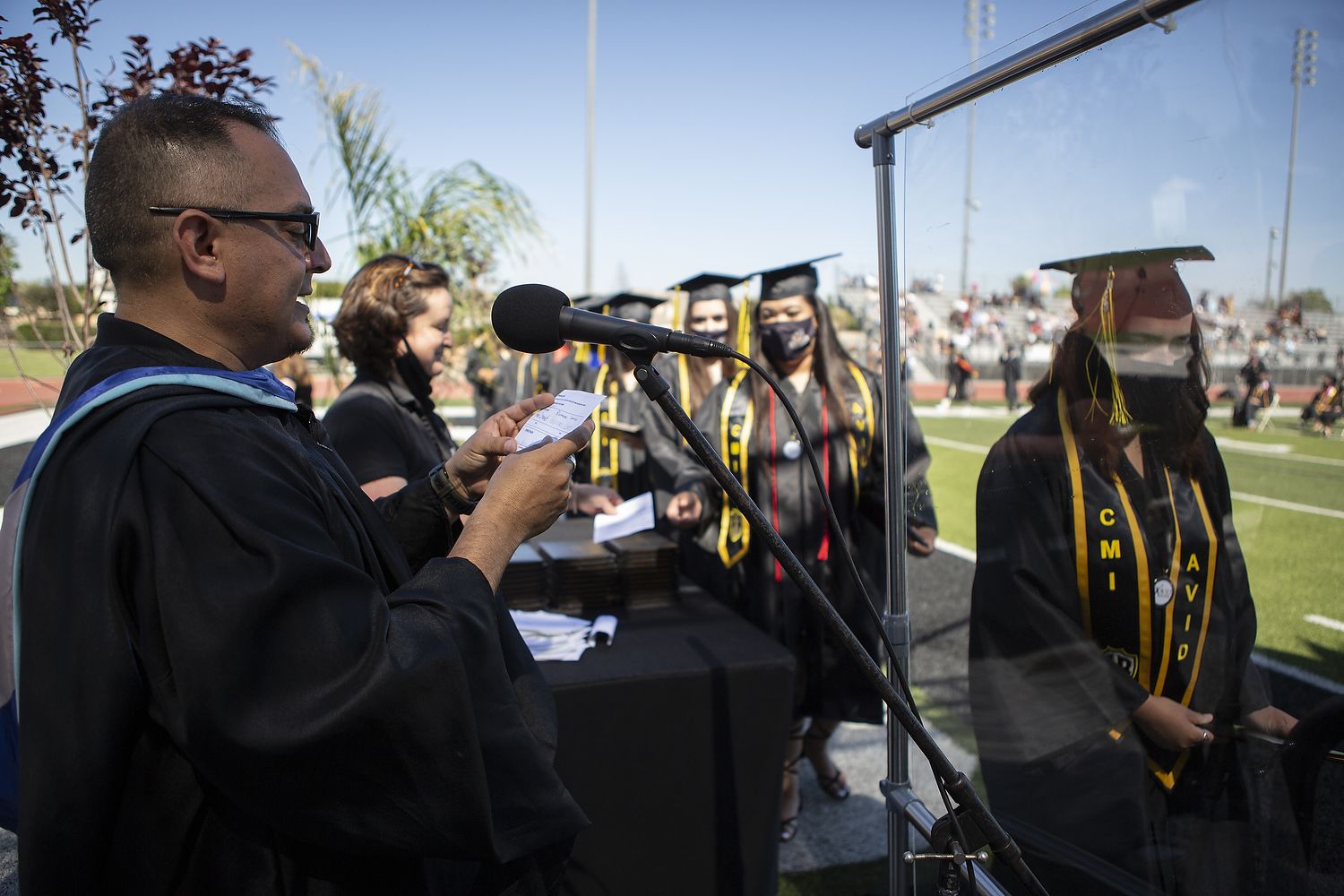 Man in academic regalia reads a card.
