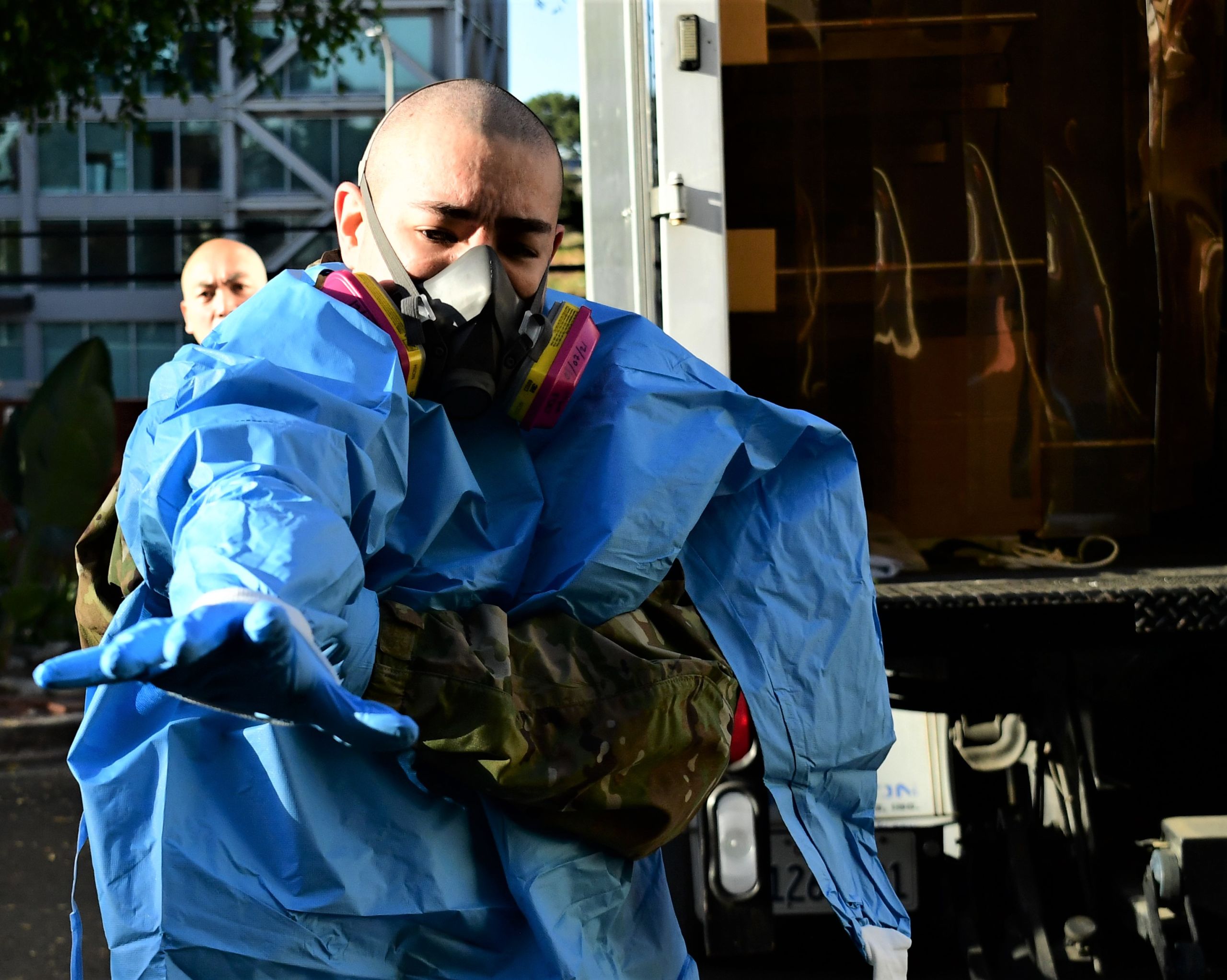Airman dawns blue protective hospital gown and latex gloves with a mask on his face.