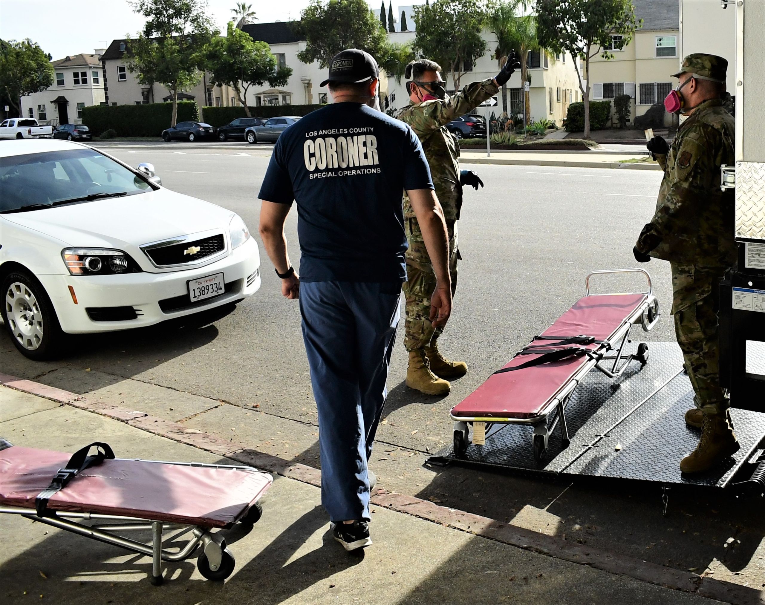 A Forensic Technician Supervisor assists California National Guardsmen in unloading wheeled stretchers.