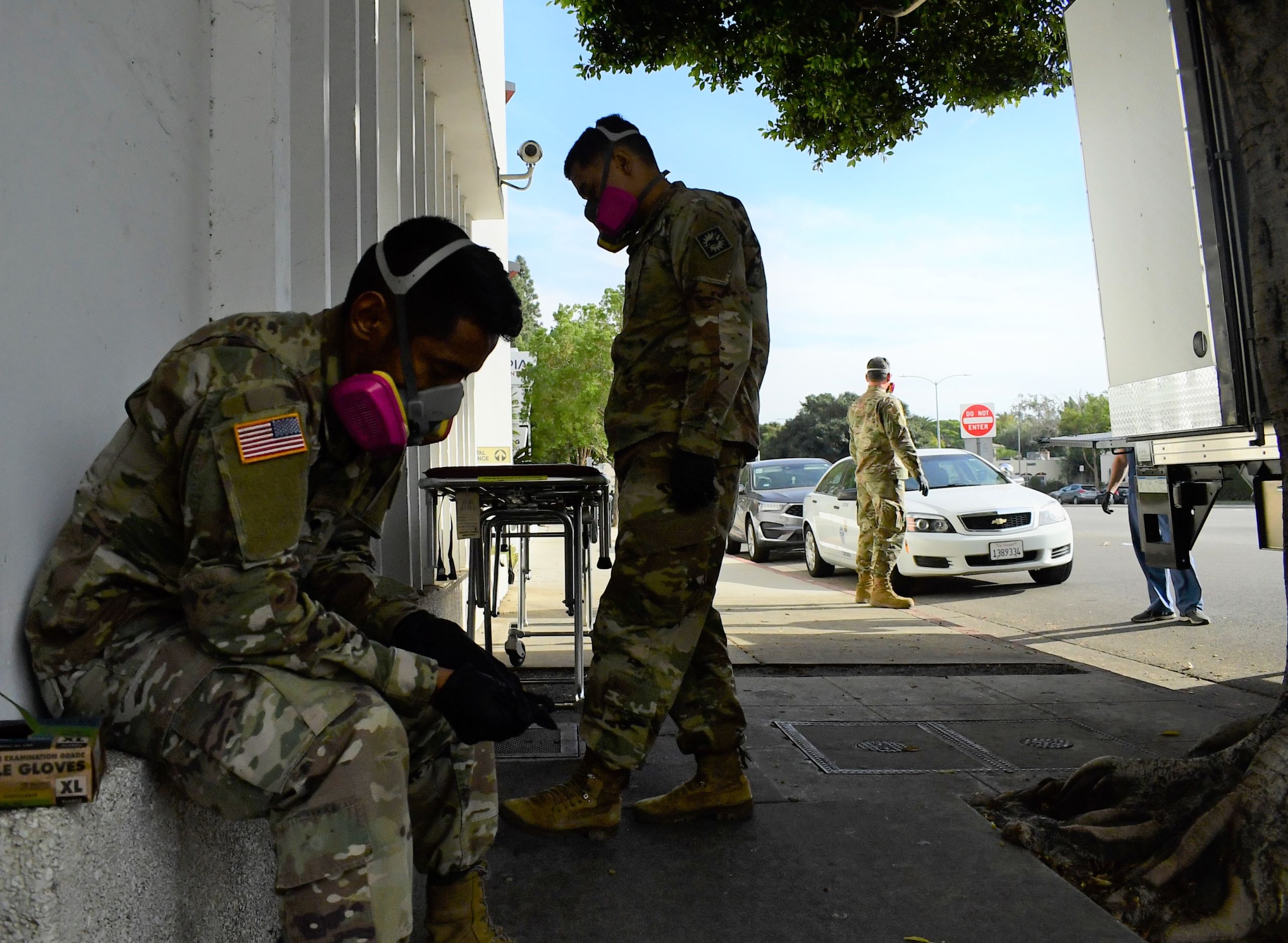 Uniformed servicemembers take a break near a wheeled stretcher on a sidewalk.