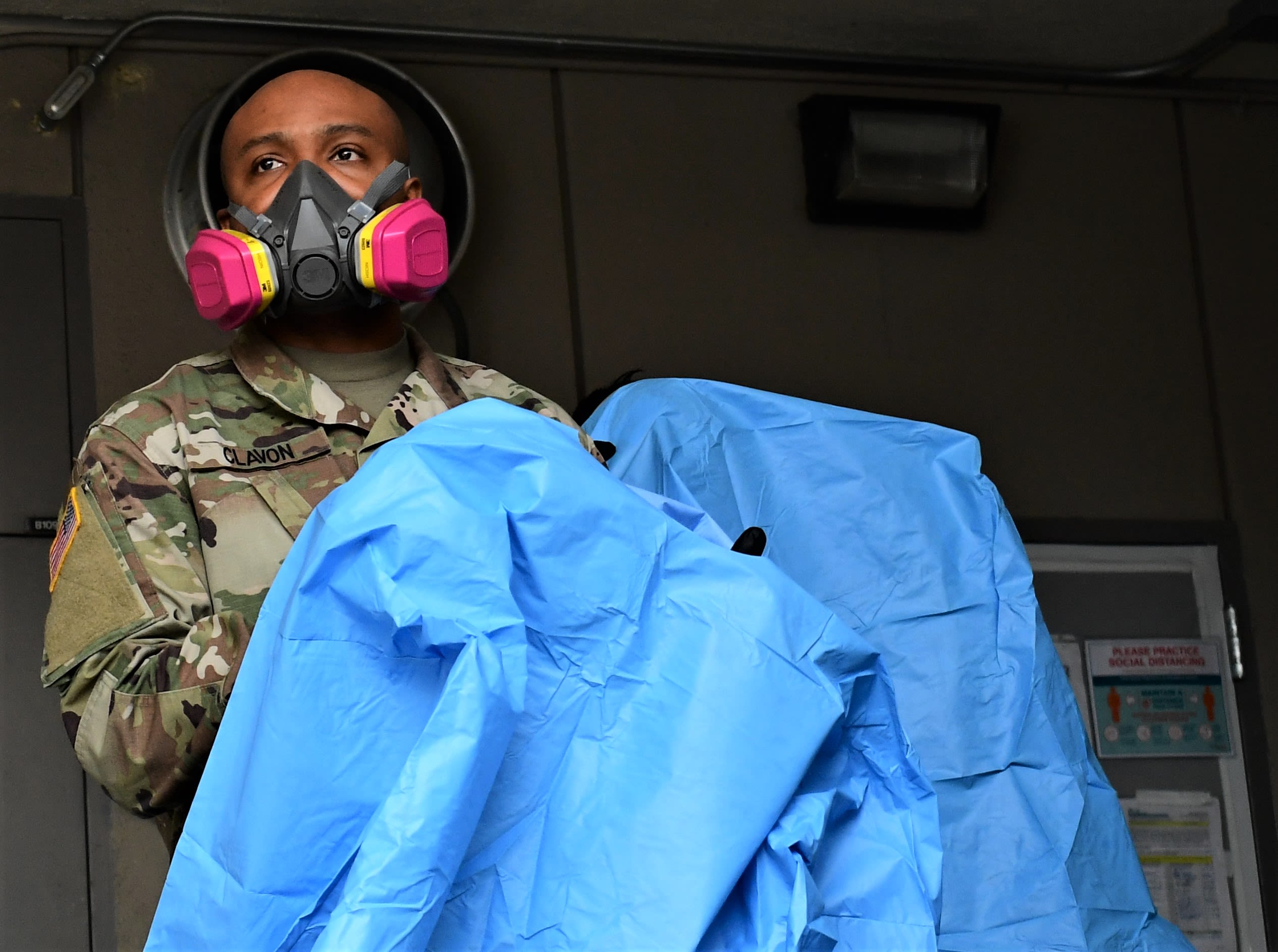 A Soldier dawns a blue disposable gown, gloves and mask.
