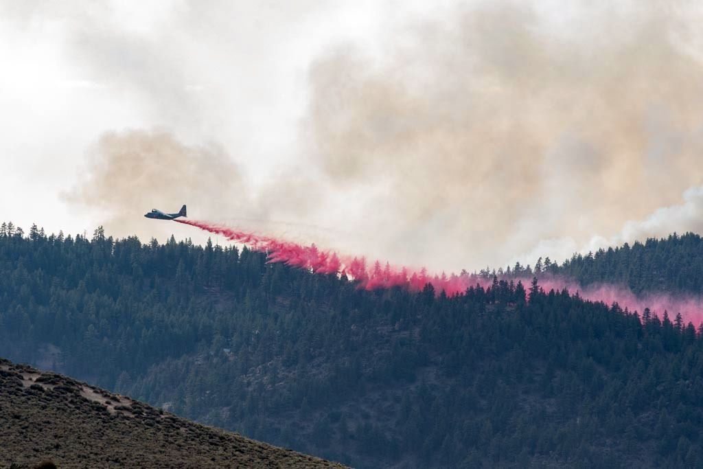 Firefighting aircraft drops red retardant on mountain.