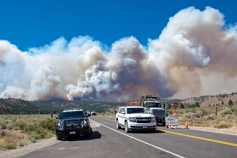 Law enforcement vehicles parked on road with smoke in background.